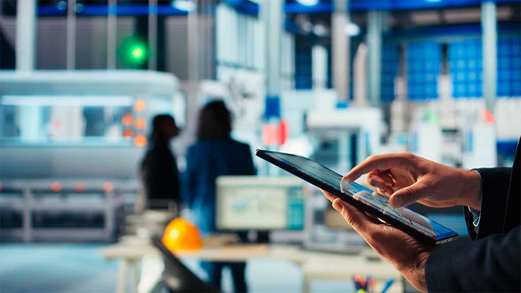 Pessoa usando tablet em ambiente corporativo com fundo de escritório moderno e pessoas ao fundo, representando multicanalidade b2b na indústria